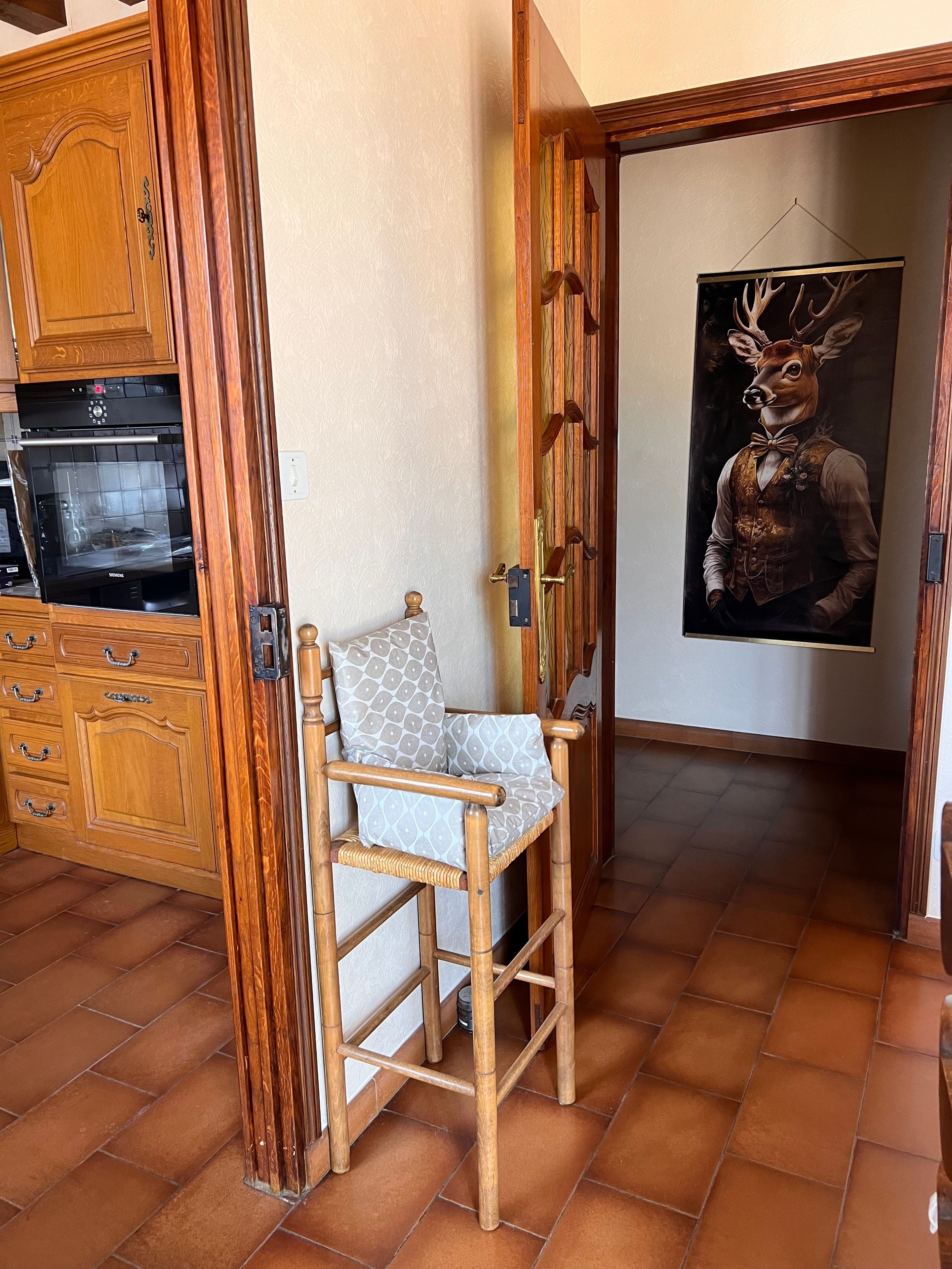 Een houten stoel met een gekleurd kussen in een kamer met betegelde vloeren en houten kasten.