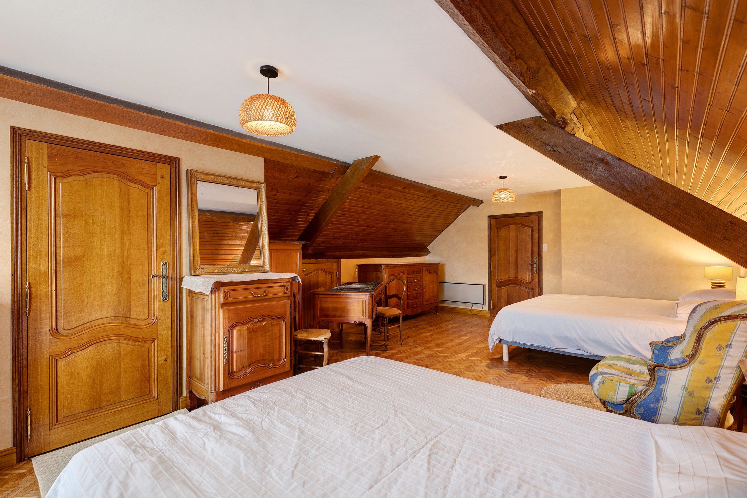 Een slaapkamer met een schuine kap, houten meubels en een bed met een witte dekbedovertrek.