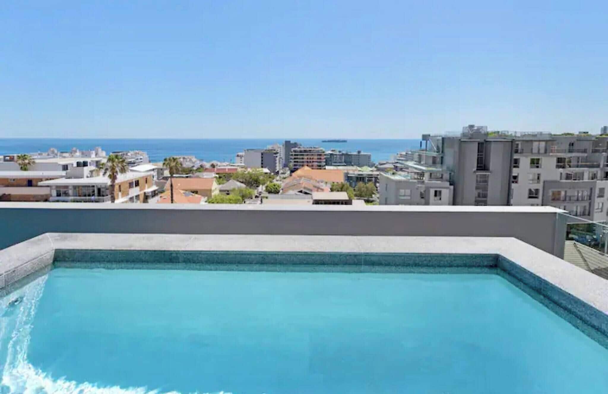 A rooftop pool with a view of the sea and surrounding buildings.
