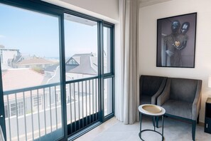 A room with a large sliding glass door leading to a balcony, a framed artwork on the wall, a grey sofa, and a small round table. - Room-oceanfront Bliss With Breathtaking (Cape Town)