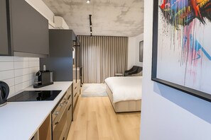A modern hotel room with a kitchenette, a bed, and a large abstract painting. - Room-oceanfront Bliss With Breathtaking (Cape Town)
