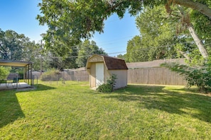 A backyard with a small shed, a covered patio area, and a wooden fence. - Extended East Tulsa Home w/ Fenced Yard (Tulsa)