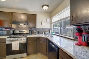 A kitchen with a stove, oven, microwave, and dishwasher. There is a window with blinds and a view of the outdoors. - Extended East Tulsa Home w/ Fenced Yard (Tulsa)