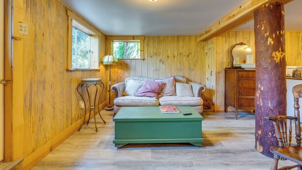 A cozy room with wooden walls, a green ottoman, a sofa, a lamp, and a wooden chair. - Yuba River Retreat for 2! Near Swimming Holes (Washington)