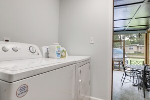 A laundry area with a front-loading washer and dryer, a bottle of laundry detergent, and a window with a view of a residential area.