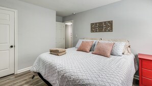 A bedroom with a bed, pillows, a blanket, a red dresser, and a door.