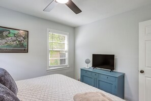 A bedroom with a bed, a dresser, a television, a ceiling fan, a window with blinds, and a framed picture on the wall.