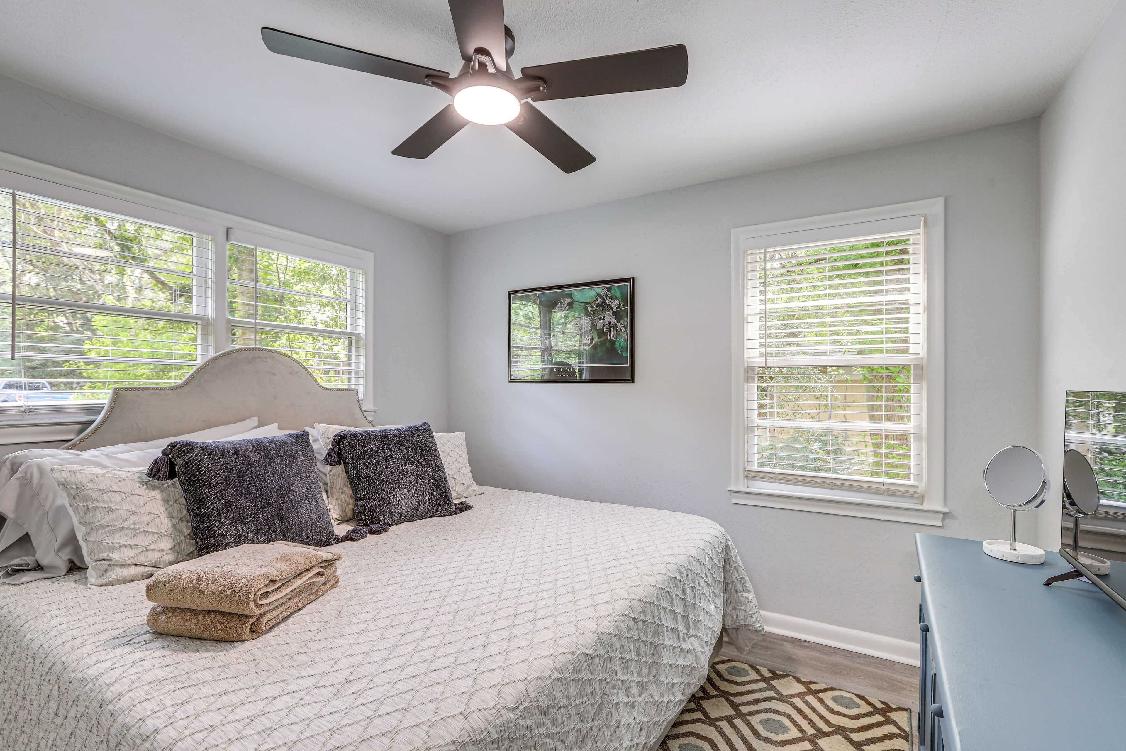 A bedroom with a bed, a ceiling fan, a window with blinds, and a framed picture on the wall.