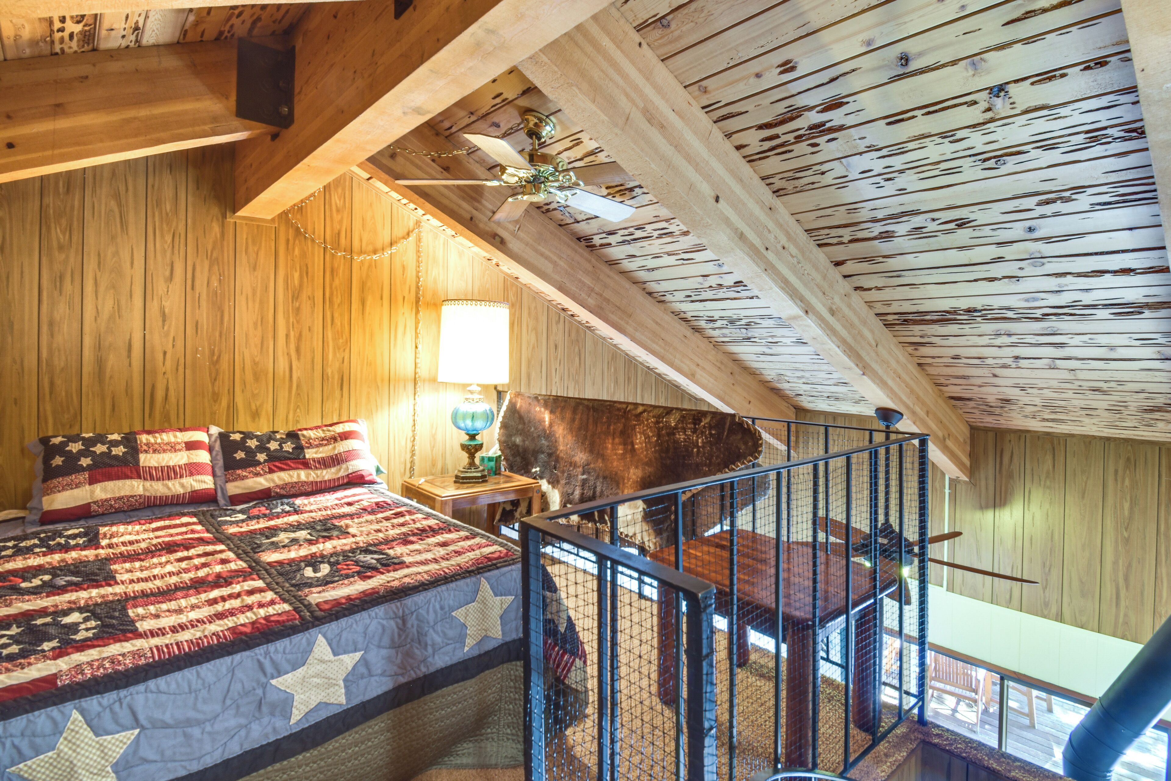 A bedroom with a wooden ceiling, a bed with a quilt, a nightstand, and a lamp.
