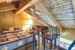 Une chambre avec un plafond en bois, un lit recouvert d’une courtepointe, une table de chevet et une lampe.