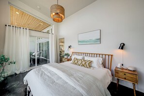 Een moderne slaapkamer met een groot bed, een houten hoofdbord, een nachtkastje en een hanglamp.