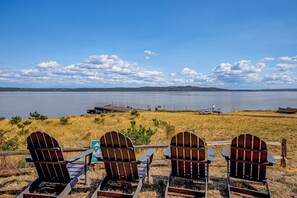 Drie Adirondack stoelen gericht op een meer met een verre oever en een heldere lucht.