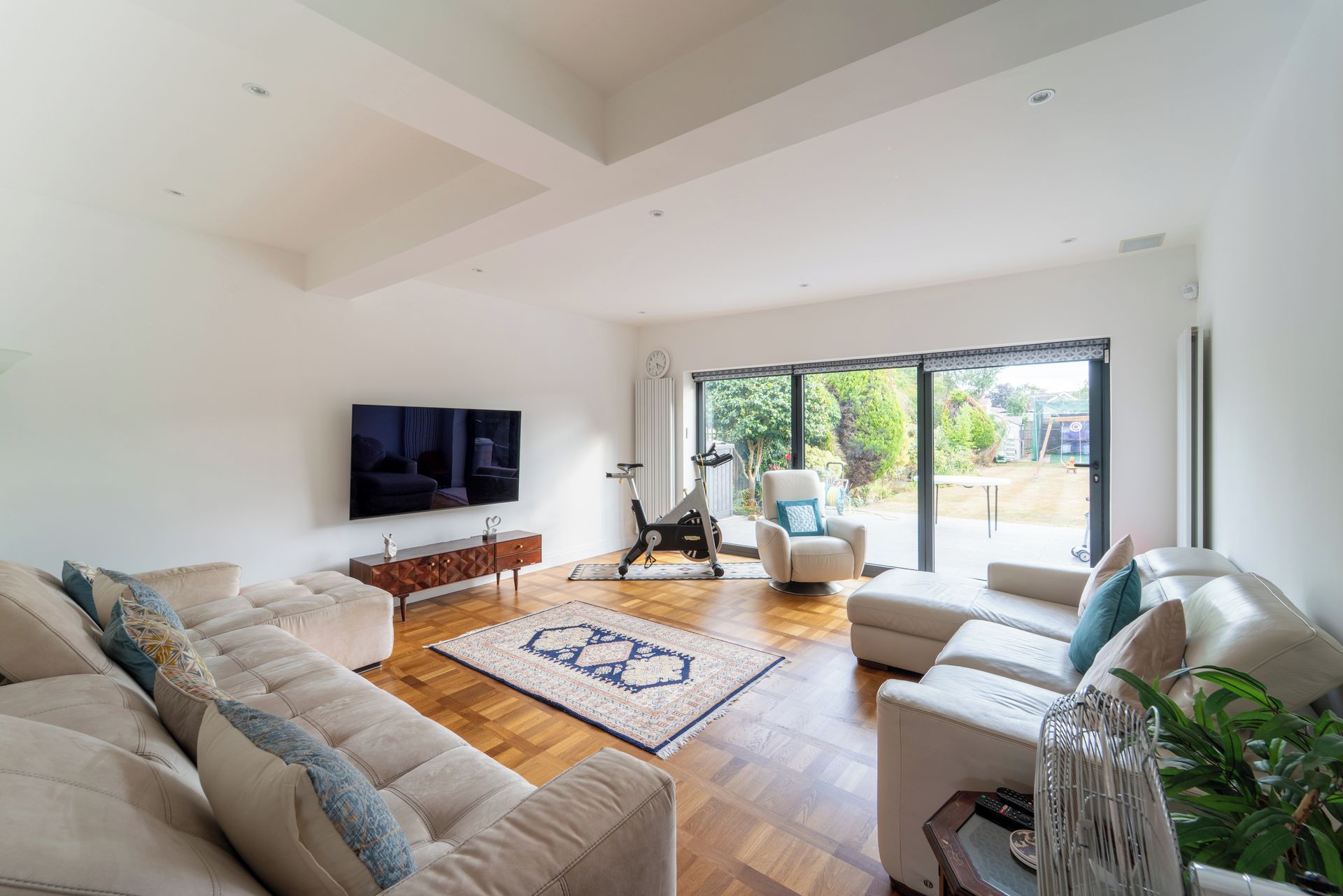A spacious living room with a large TV, a sofa, a chair, and a view of the outdoors through a sliding glass door.