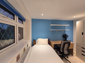 A bedroom with a bed, a desk, a chair, a radiator, and a window with blinds.