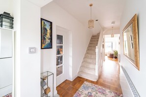 A hallway with a staircase, a framed painting, a glass cabinet, and a floral rug. - Extended Family Home with Parking near Heathrow (Ickenham)