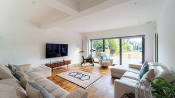 A spacious living room with a large TV, a sofa, a chair, and a view of the outdoors through a sliding glass door.