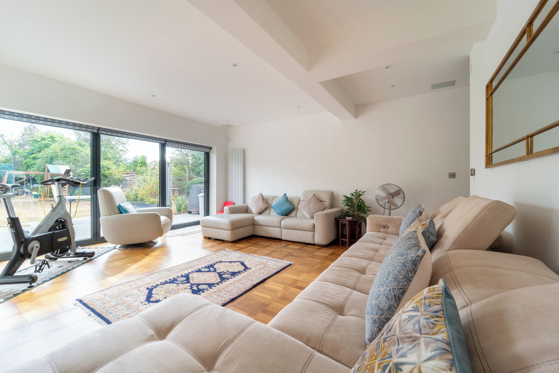A spacious living room with a large window, a sofa set, a standing fan, and an exercise bike.
