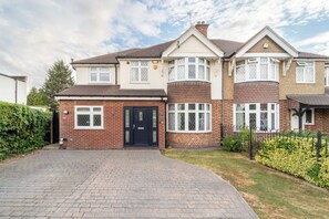 A two-story residential house with a brick facade, a black front door, and a paved driveway.