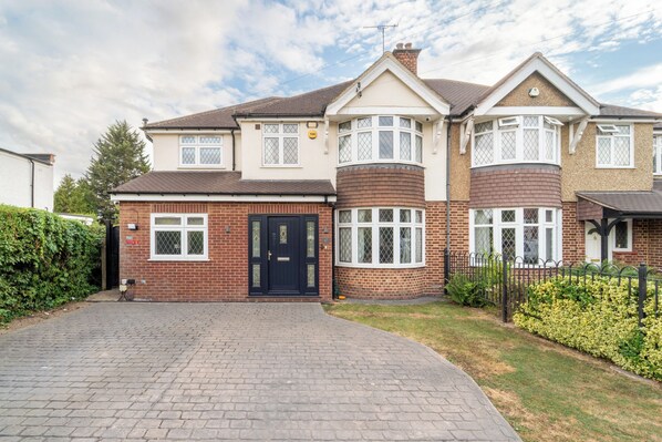 A two-story residential house with a brick facade, a black front door, and a paved driveway.