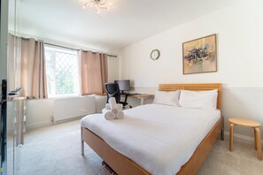 Ein Hotelzimmer mit einem Bett, einem Schreibtisch mit Computer, einem Sessel, einem kleinen Tisch, einer Uhr und einem Fenster mit Vorhängen.