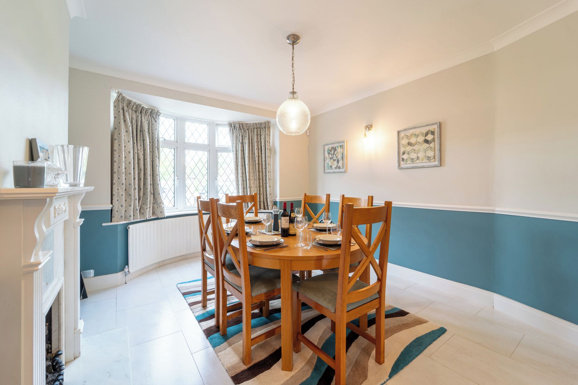 A dining area with a round table, chairs, a chandelier, and a window with curtains.