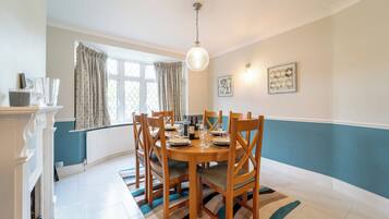 A dining area with a round table, chairs, a chandelier, and a window with curtains.