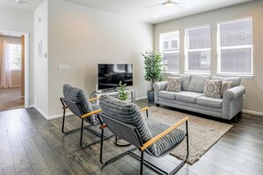A living room with a grey sofa, two armchairs, a flat-screen TV, a potted plant, and a large window with blinds. - 2BR, 2BA, 2Car - Office, Laundry, Quiet, by DIA (Denver)