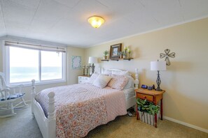 Een slaapkamer met een bed, een stoel, een nachtkastje, een lamp, een wandplank met decoratieve objecten, en een raam met uitzicht.