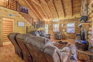 Ein Holzblockhaus-Interieur mit Treppe, Ledersesseln, einem Chandelier und rustikalen Einrichtungsgegenständen.