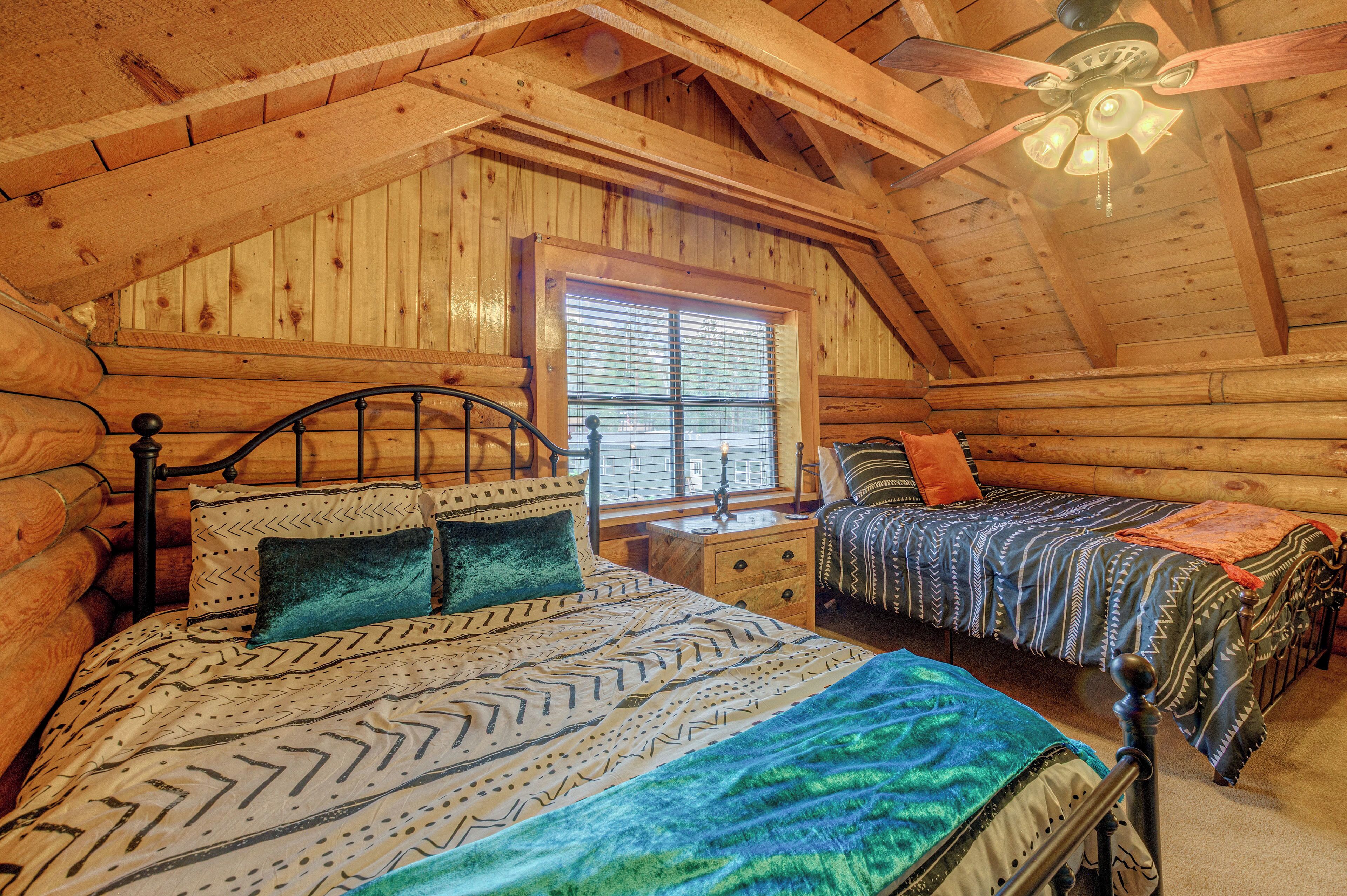 A log cabin bedroom with a loft-style ceiling, a bed with patterned bedding, a nightstand, and a window with blinds.