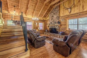A log cabin interior with a fireplace, leather sofas, a stone wall, and a wooden staircase. - 8 Mi to Ruidoso Downs! Family Cabin w/ Deck & Yard (Ruidoso)