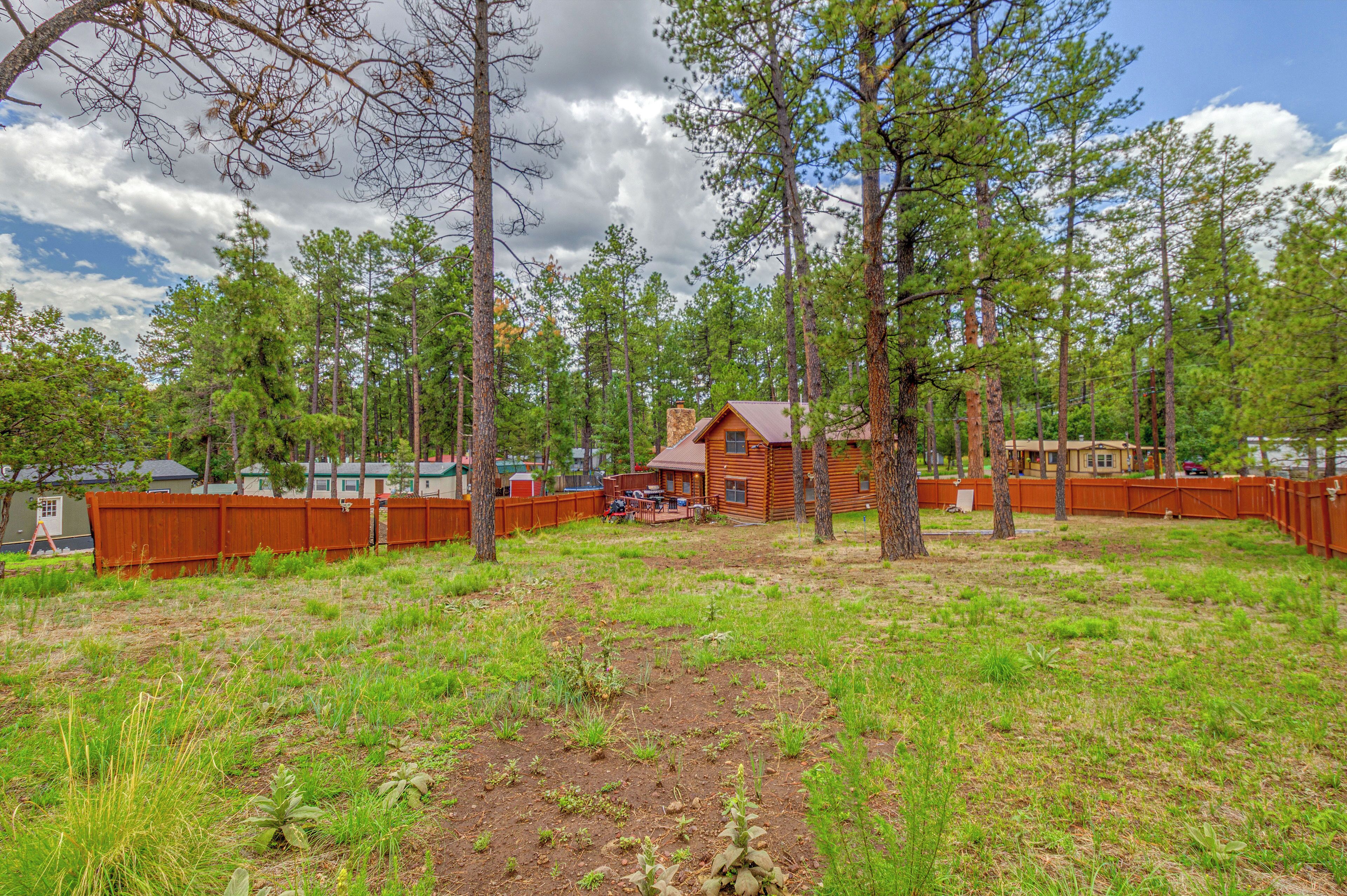 A cabin surrounded by a wooden fence, with a grassy yard and trees in the background.