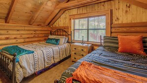 Quarto de cabana de madeira com duas camas, teto de madeira e janela com persianas.