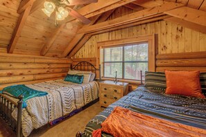 Ein Schlafzimmer in einer Blockhütte mit zwei Betten, Holzbalkendecke und einem Fenster mit Jalousien.