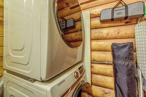 Une machine à laver Samsung dans une pièce aux murs en bois, avec un sac à linge suspendu.