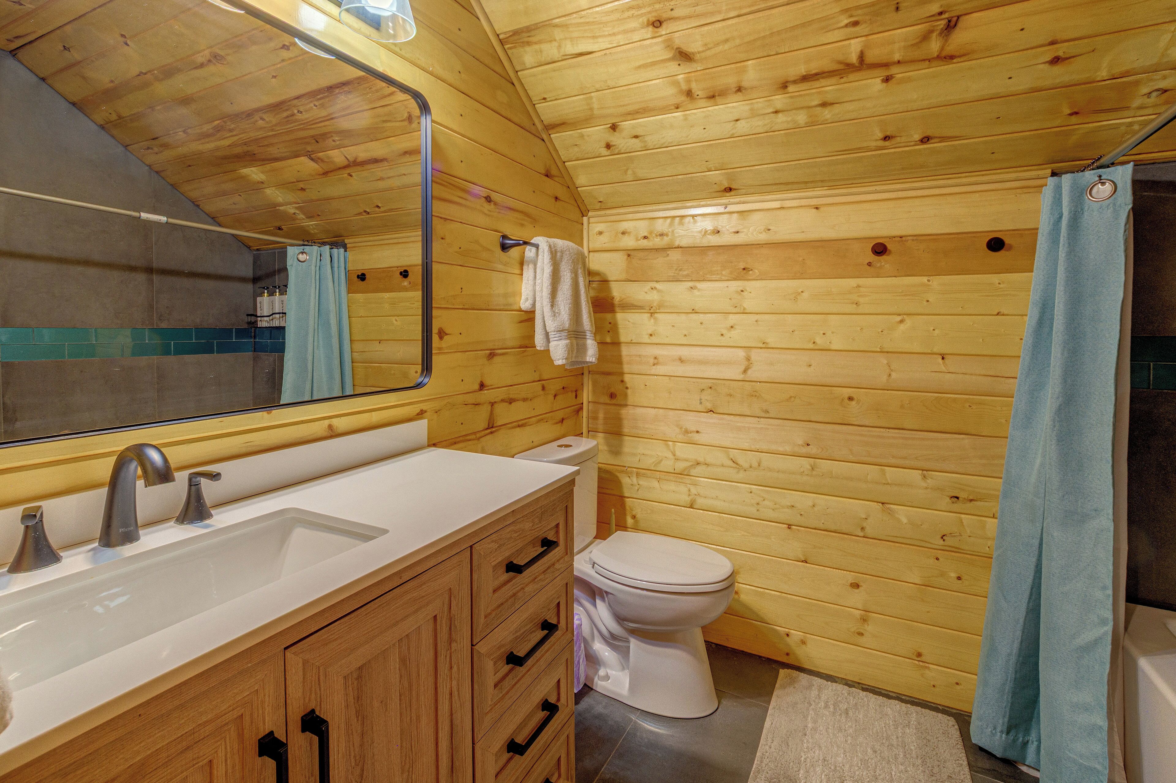 A wooden cabin bathroom with a sink, toilet, and shower curtain.
