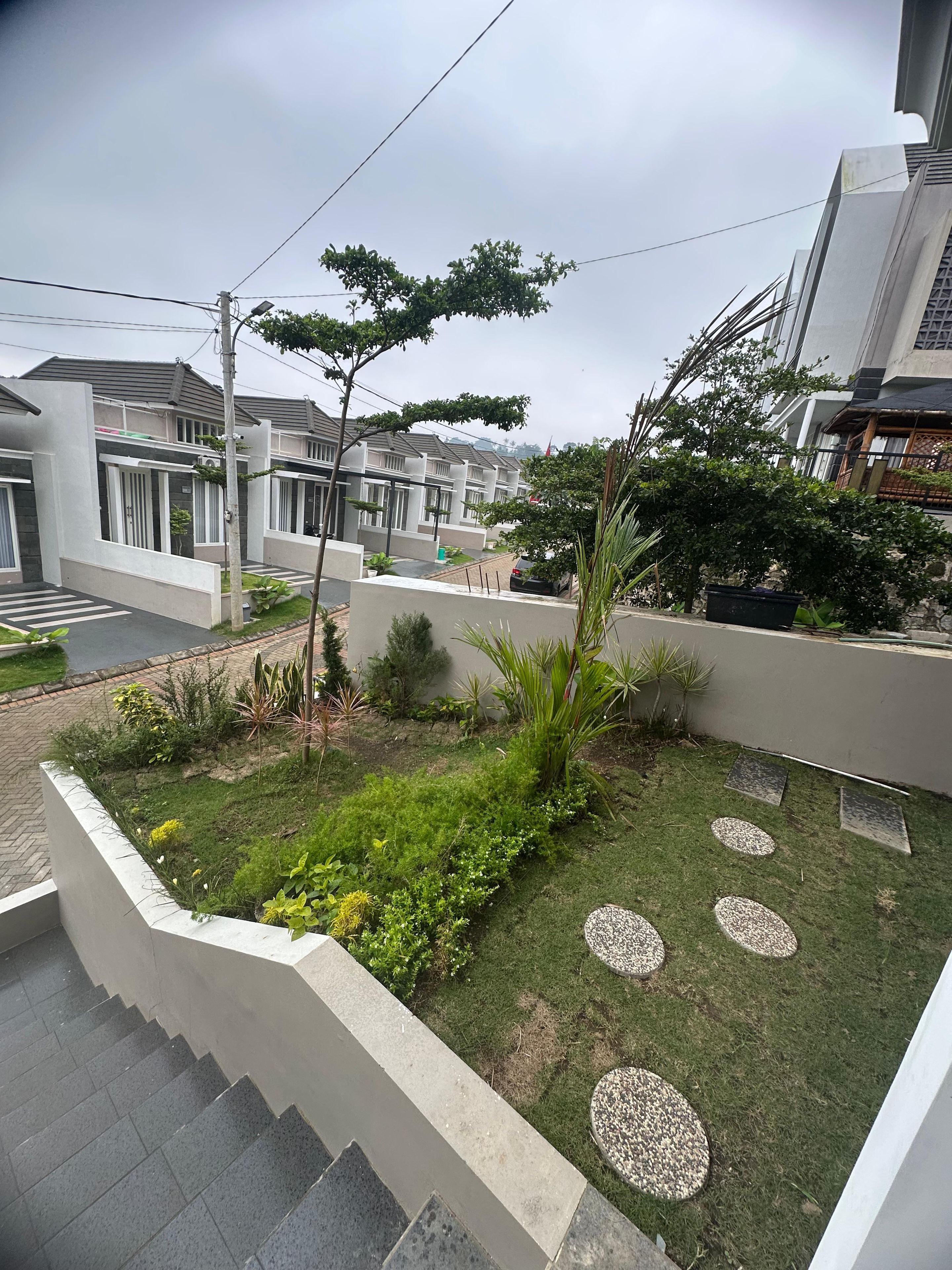 Un quartier résidentiel avec des maisons modernes, un jardin verdoyant agrémenté de pas japonais et un escalier menant à un niveau supérieur.