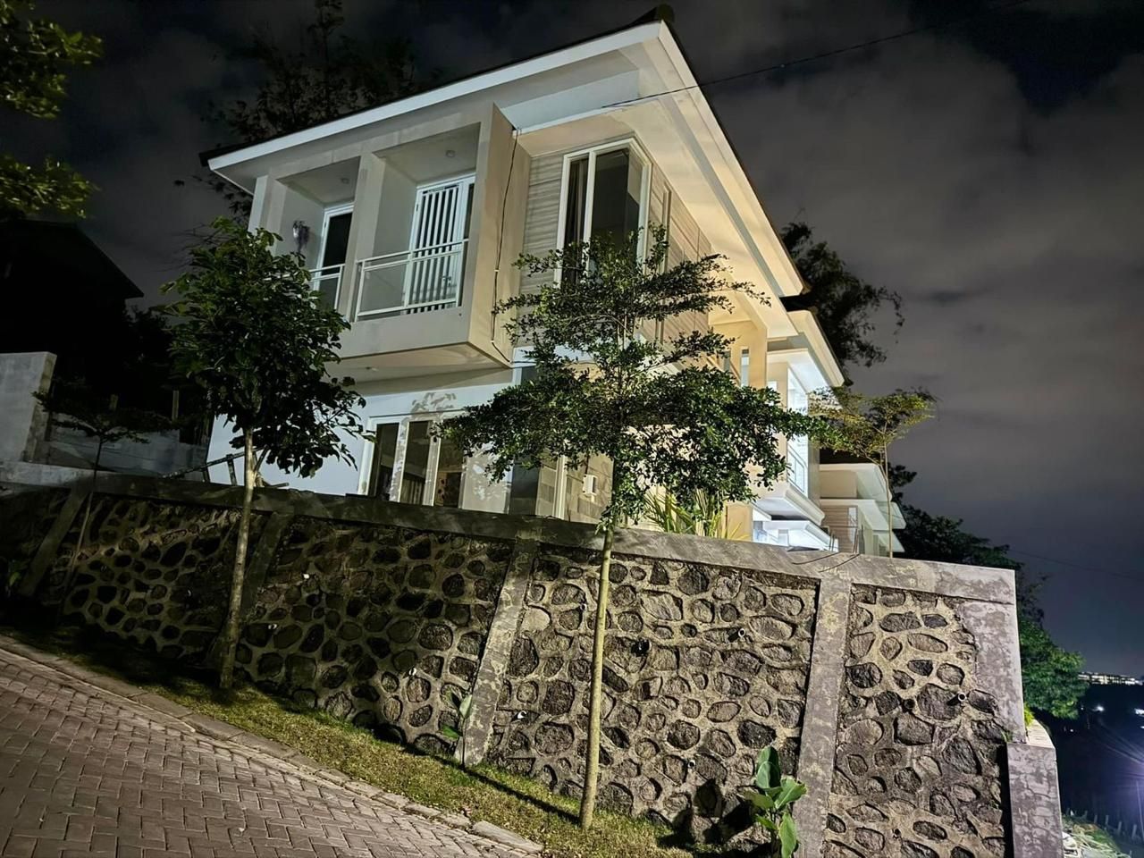 A two-story house with a stone wall in front, a paved driveway, and a tree.