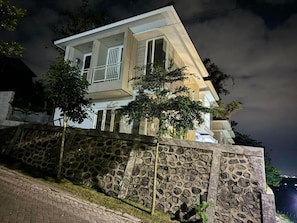 Une maison à deux étages, avec un mur de pierre à l’avant, une allée pavée et un arbre.