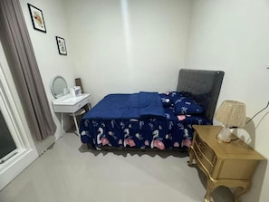 A bedroom with a bed, bedside table, lamp, and a dresser.
