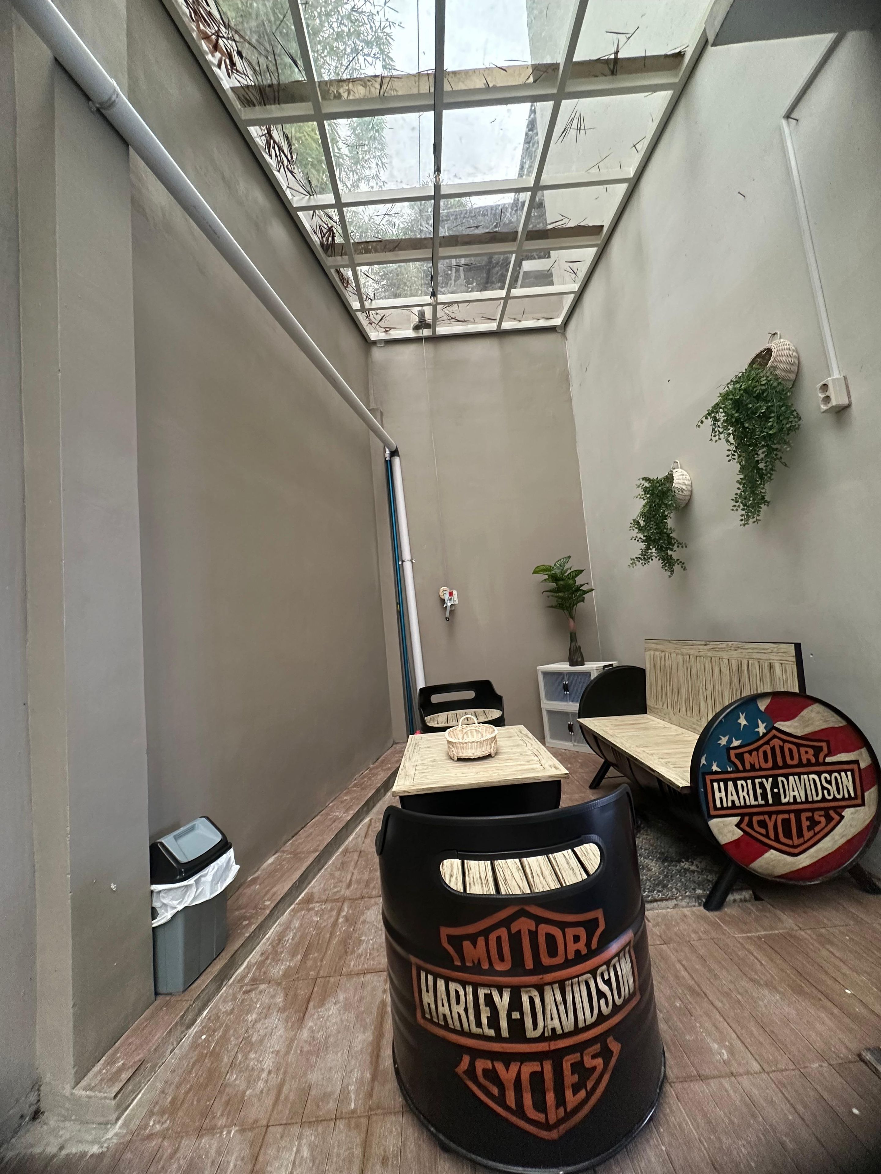 Um corredor estreito com um claraboia, uma mesa com um cesto, um barril Harley-Davidson e uma cama com o logotipo Harley-Davidson.