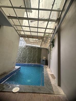 A small indoor swimming pool with a tiled floor and a glass ceiling.