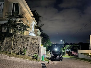 Une rue résidentielle la nuit, avec une voiture garée, un mur de pierre et un immeuble doté d’un balcon.