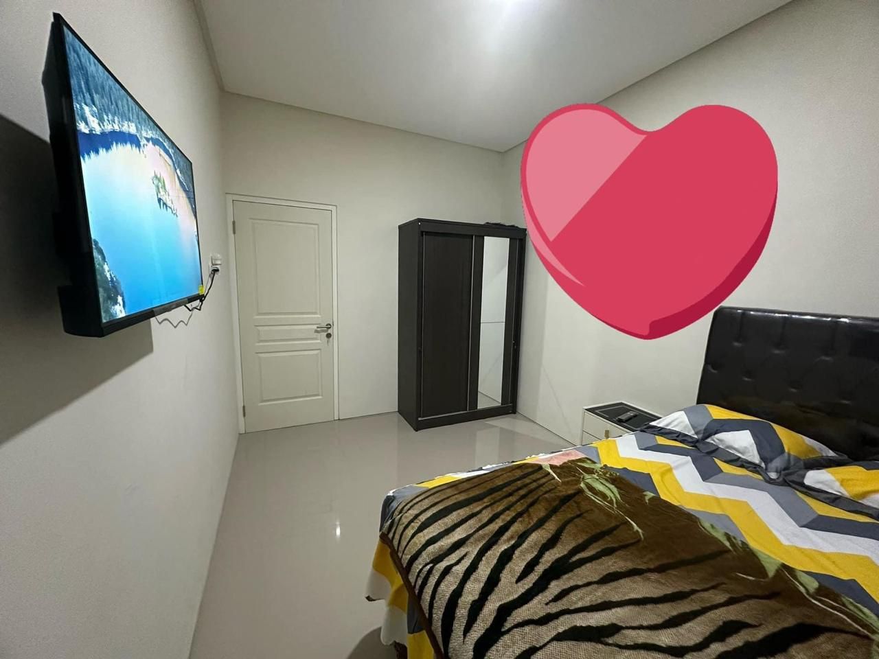 Un dormitorio con cama, televisor en la pared, armario y puerta.