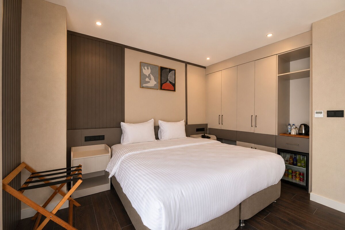 A modern bedroom with a large bed, a wardrobe, a radiator, and a small seating area.