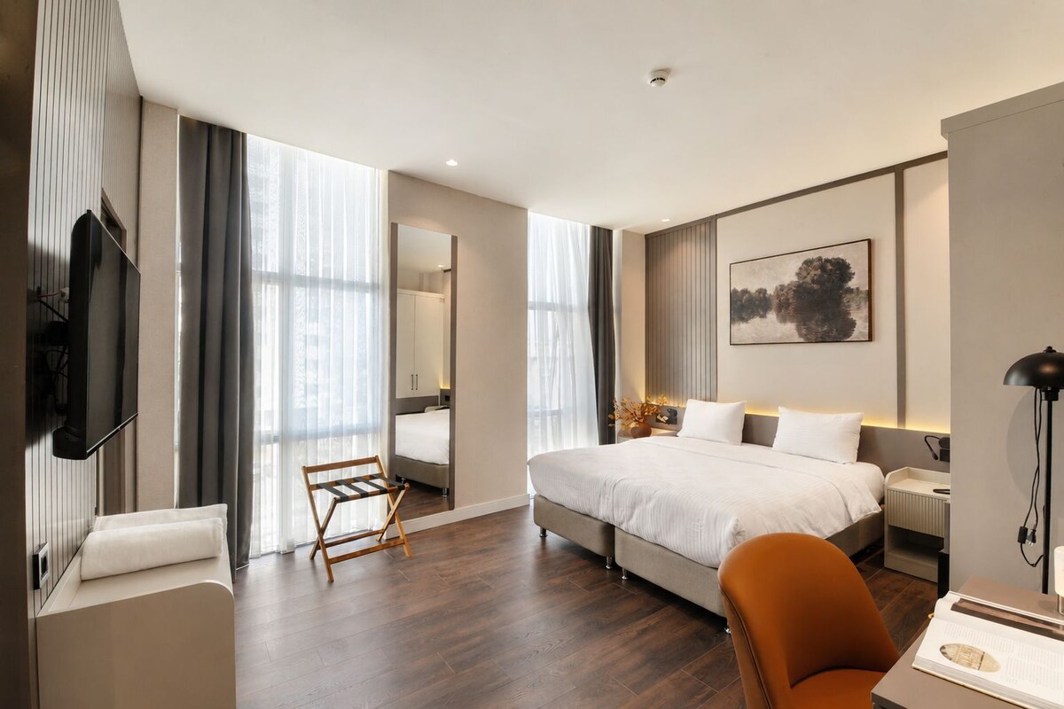 A modern hotel room with a large bed, a desk, a chair, and a television.