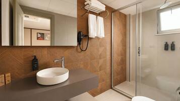 Un bany modern amb un mirall gran, un lavabo rodó, una dutxa amb porta de vidre i un vàter.