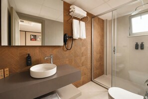 Ein modernes Badezimmer mit einem großen Spiegel, einem runden Waschbecken, einer Dusche mit Glastür und einer Toilette.