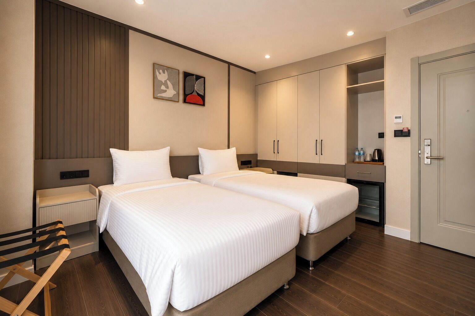 Habitació d'hotel amb dos llits, una taula de treball, una cadira, un armari i una cuineta.
