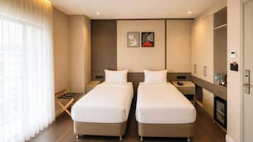 A hotel room with two beds, a wardrobe, a bedside table with a phone, and a window with curtains.